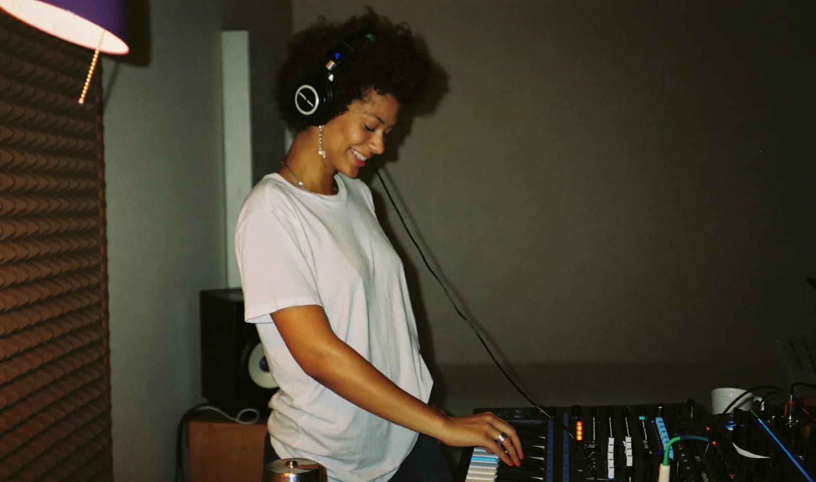 Music producer smiling while playing a synthesizer in her bedroom studio; illustrative scene
