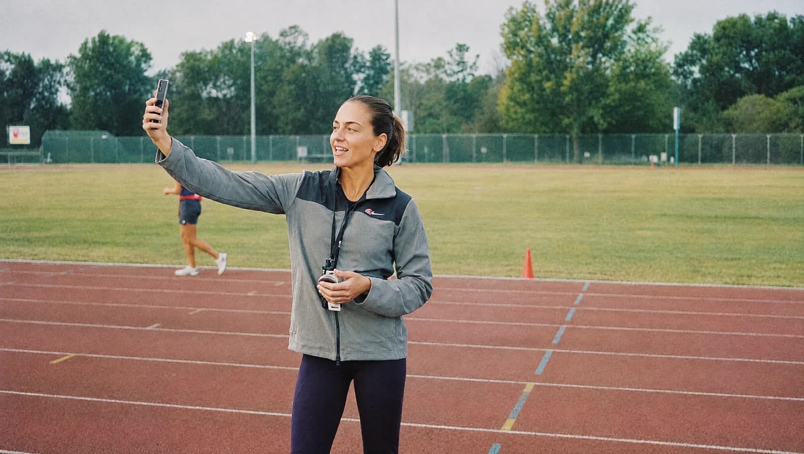Sports coach giving feedback with a stopwatch on a public running track; illustrative scene