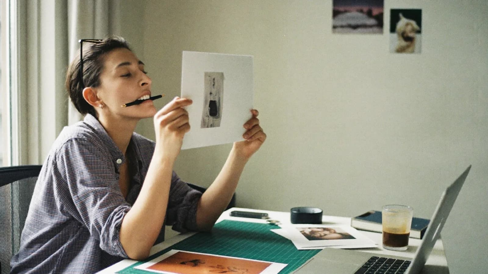 Creative director judging a printed photo proof at her desk, pen between her teeth; illustrative scene