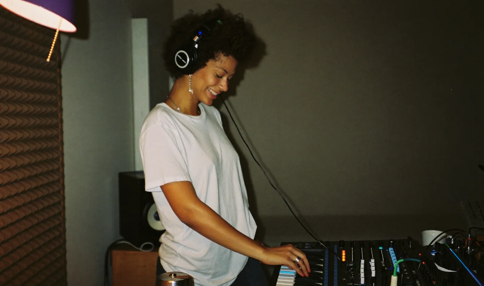 Music producer smiling while playing a synthesizer in her bedroom studio; illustrative scene