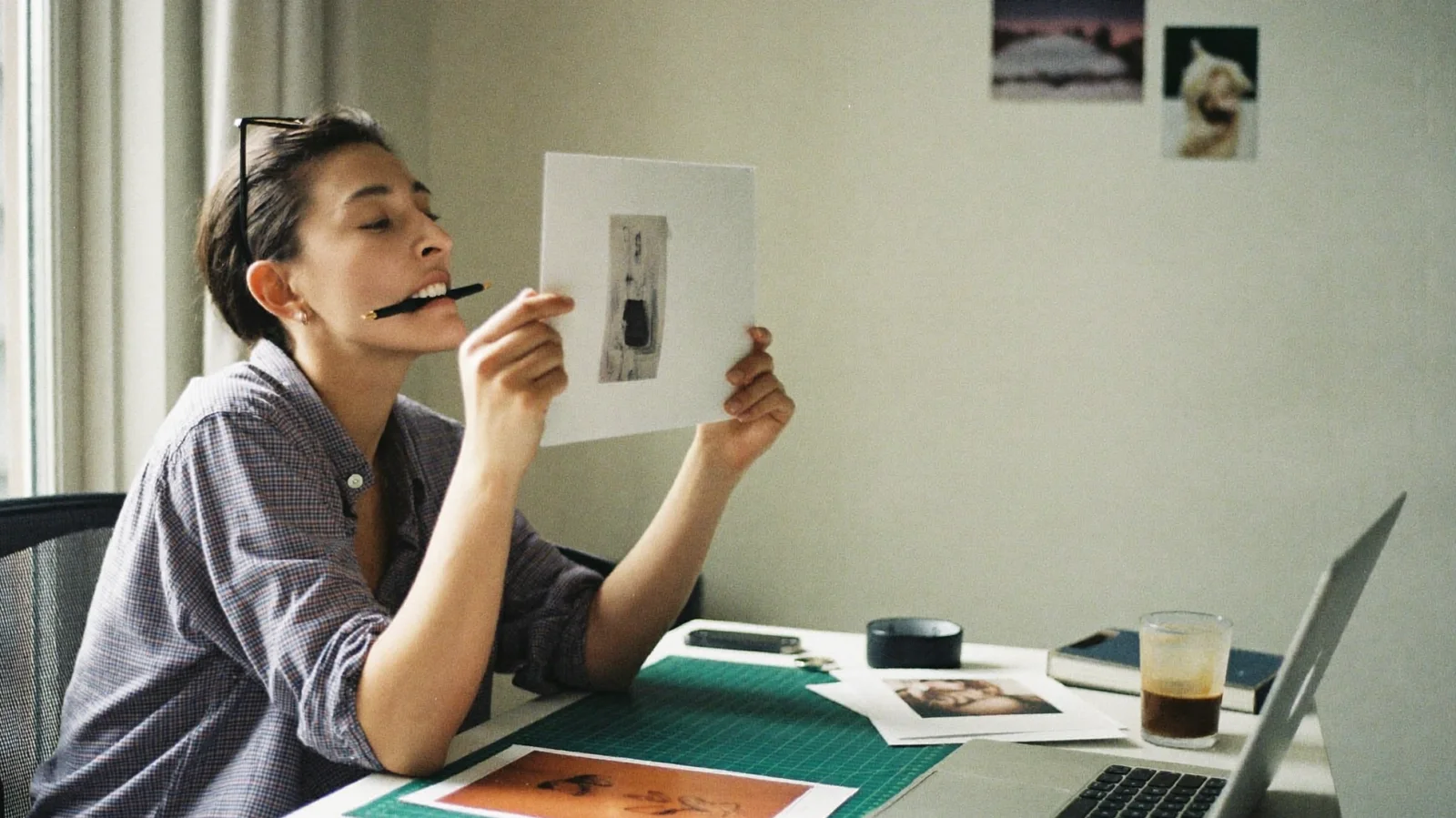 Creative director judging a printed photo proof at her desk, pen between her teeth; illustrative scene
